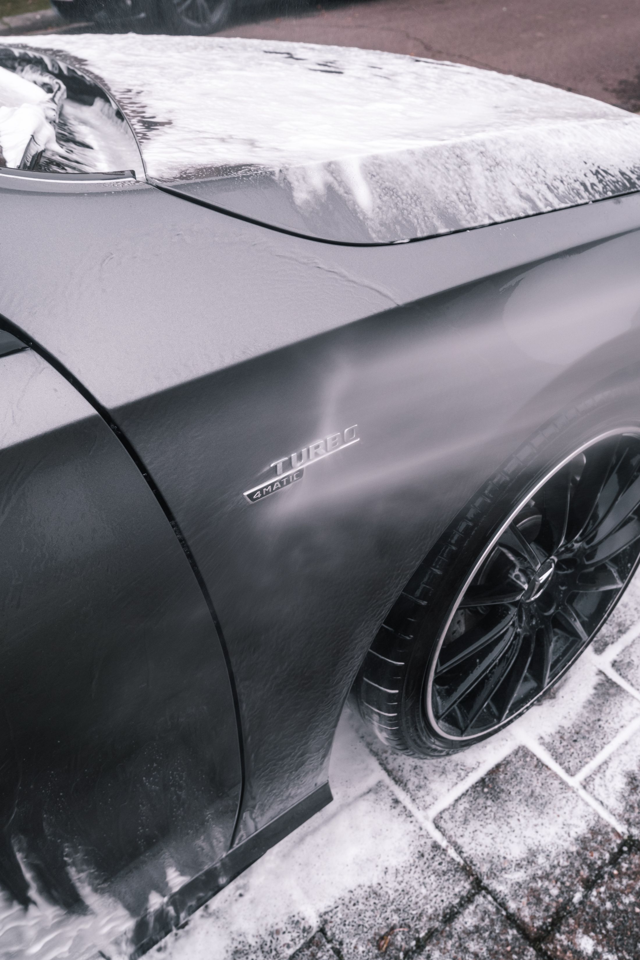 Foam covering the hood and front quarter of a dark vehicle during an exterior wash