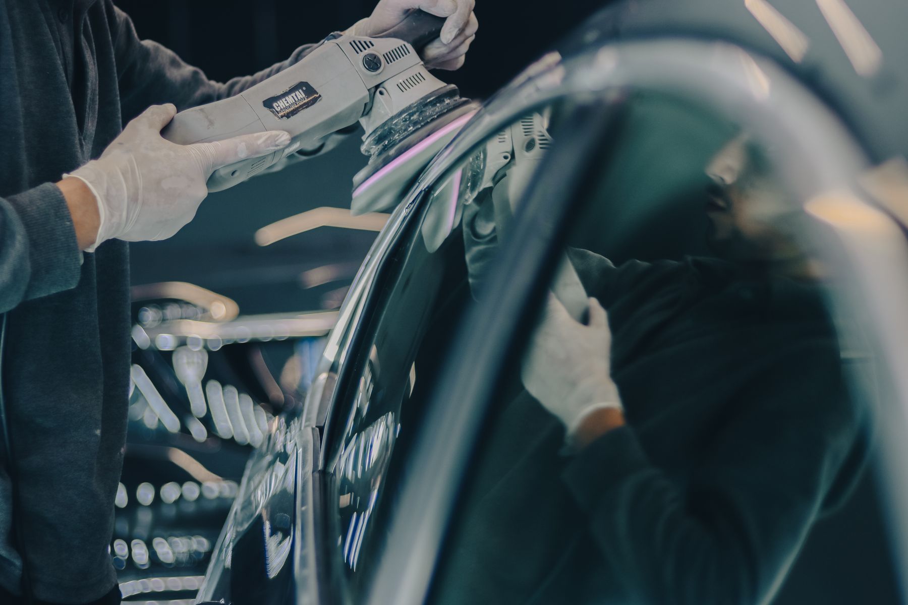 Detailing technician polishing a reflective black vehicle panel