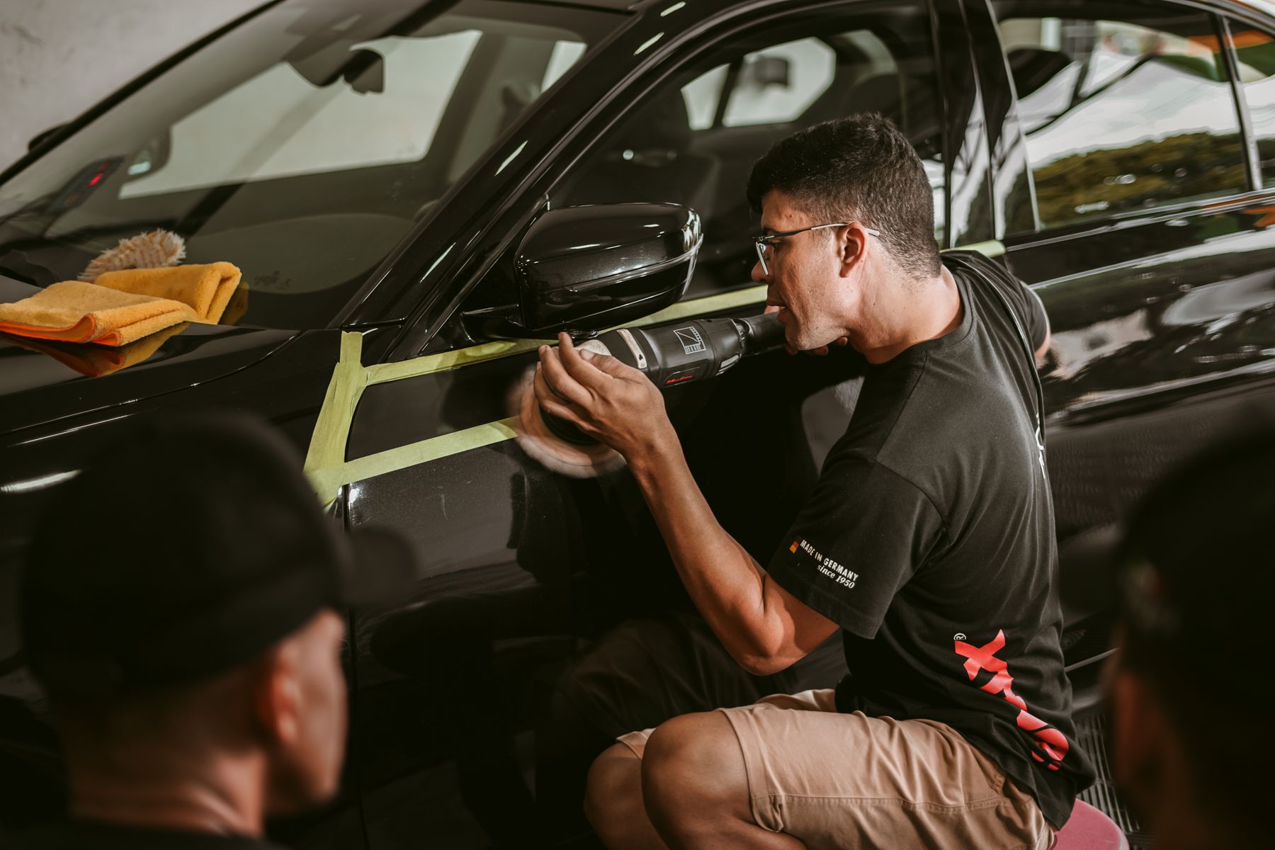 A technician using a polishing machine on the side of a black vehicle